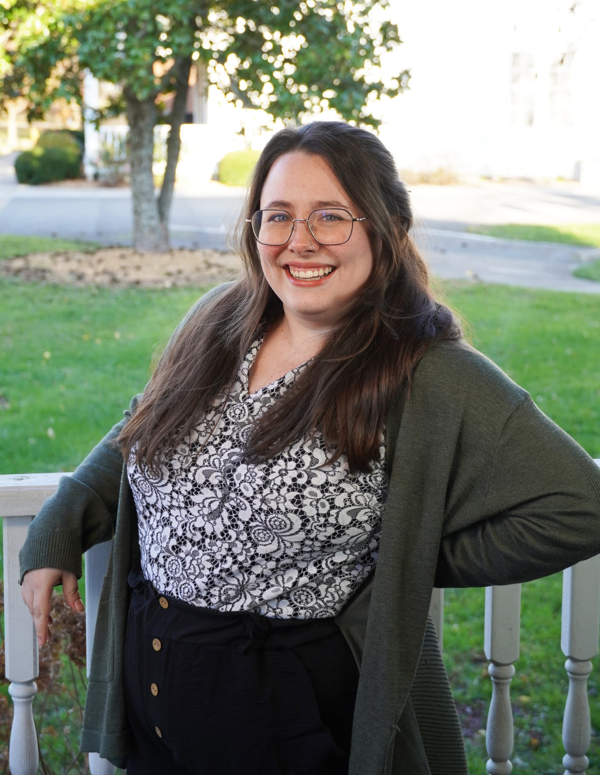 Berea College Admissions Counselor, Morgan Hudson Mecham, leaning against a white fence, with green grass and a tree in the background.