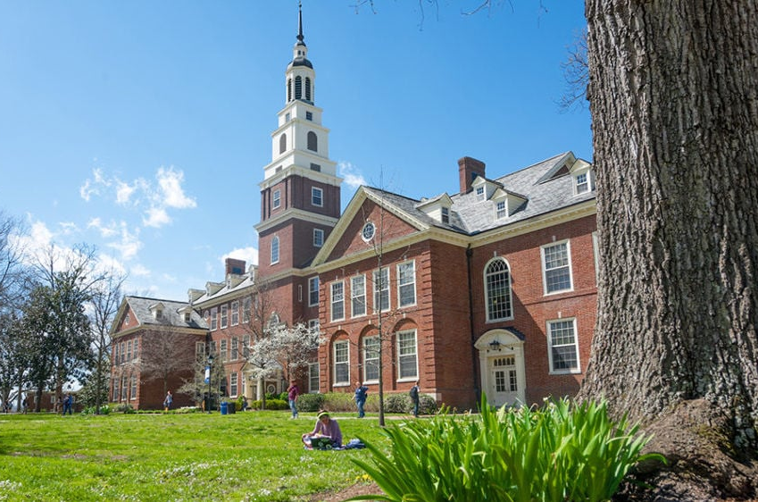 Brick college building on Berea campus during spring with students sitting on the green lawn.