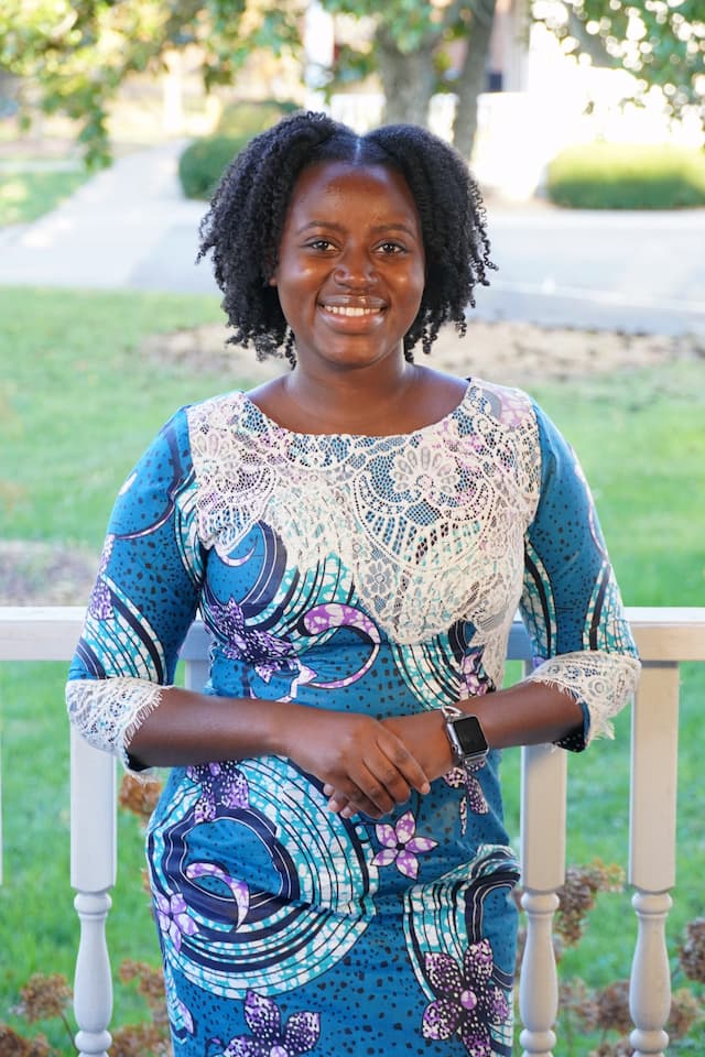 Berea College Admissions Counselor, Edithe Rose, leaning against a white fence, with green grass and a tree in the background.